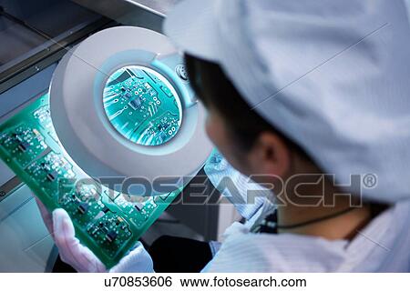 Stock Photograph - Worker at small parts manufacturing factory in China looking through magnifier at microchips. Fotosearch