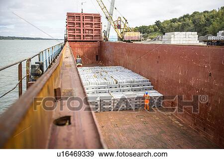 Stock Photo - Worker checking metal ingots in ship's hold. Fotosearch