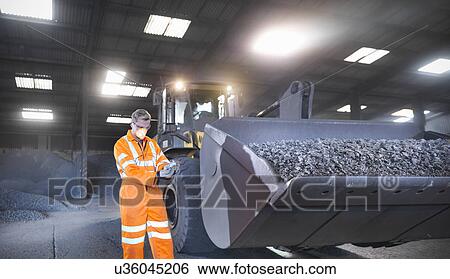 Stock Photograph - Worker in mineral store inspecting handful of metal alloy next to digger. Fotosearch