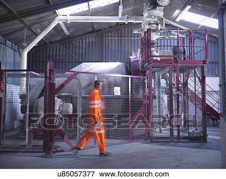 Stock Photo - Worker in reflective clothing passing machinery in zircon flour mill. Fotosearch