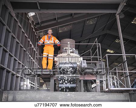 Stock Photo - Worker in reflective workwear operating metal crushing machine. Fotosearch