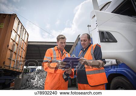 Stock Image - Worker inspecting delivery paperwork with truck driver. Fotosearch