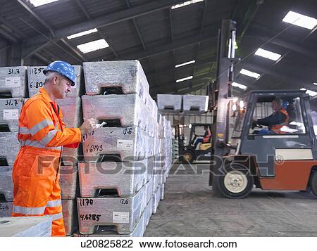 Stock Image - Worker inspecting metal alloy store in port. Fotosearch