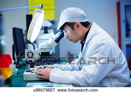 Stock Photo - Workers at small parts manufacturing factory in China looking through microscope. Fotosearch