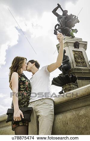 Picture - Young couple beside statue, kissing and taking self portrait photograph. Fotosearch