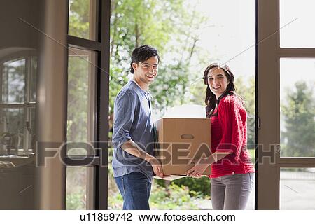 Stock Image - Young couple carrying cardboard box into new house. Fotosearch