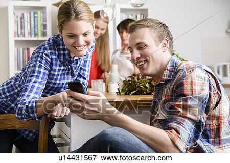 Young couple in kitchen with cell phone View Large Photo Image Stock Photo - Young couple in kitchen with cell phone. Fotosearch