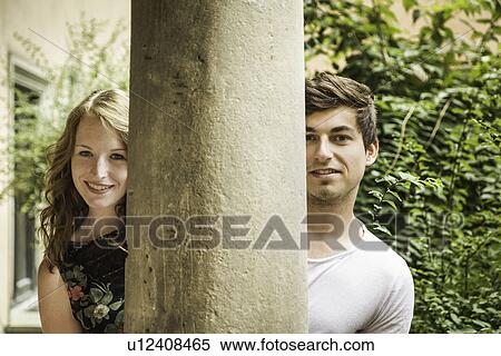 Stock Photography - Young couple looking around pillar. Fotosearch