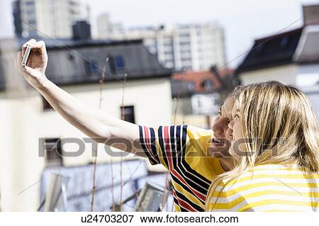 Young couple photographing themselves on rooftop View Large Photo Image Stock Photo - Young couple photographing themselves on rooftop. Fotosearch