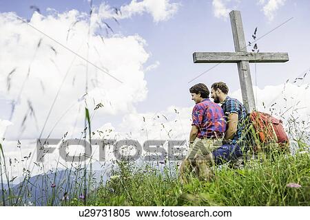 Stock Photography - Young couple sitting by cross, Tyrol, Austria. Fotosearch