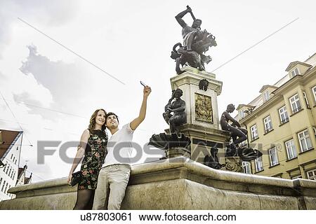 Young couple taking self portrait photograph beside statue in Augsburg, Bavaria, Germany View Large Photo Image Stock Image - Young couple taking self portrait photograph beside statue in Augsburg, Bavaria, Germany. Fotosearch