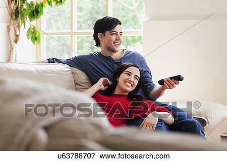 Stock Photo - Young couple watching TV on living room sofa. Fotosearch