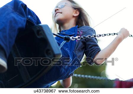 Stock Photo - Young girl playing on swing in park. Fotosearch