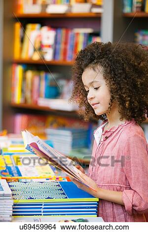 Picture - Young girl reading storybook in library. Fotosearch