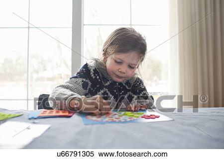 Stock Photography - Young girl sitting at table concentrating on game. Fotosearch