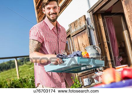 Picture - Young man carrying tray outside chalet, Tyrol, Austria. Fotosearch