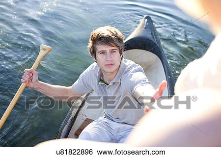 Stock Photograph - Young man in rowing boat reaching up to female friends. Fotosearch