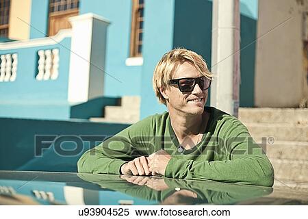 Young man leaning against blue car View Large Photo Image Stock Photography - Young man leaning against blue car. Fotosearch
