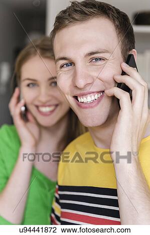 Young man on cell phone with woman in background View Large Photo Image Stock Image - Young man on cell phone with woman in background. Fotosearch