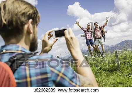 Stock Photo - Young man photographing friends, Tyrol, Austria. Fotosearch