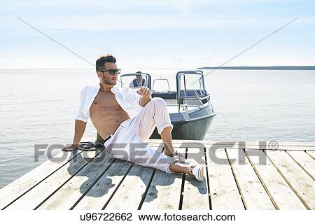 Stock Image - Young man sitting on pier, Gavle, Sweden. Fotosearch