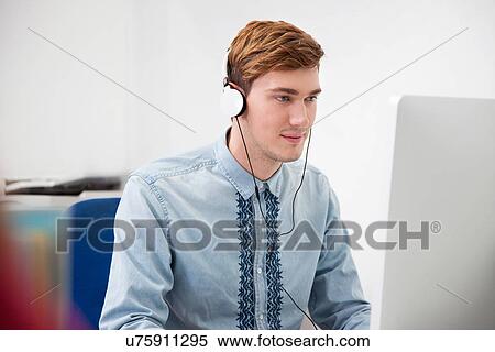 Stock Photography - Young man uwearing headphones in office. Fotosearch