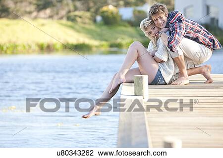 Young romantic couple sitting on pier View Large Photo Image Stock Image - Young romantic couple sitting on pier. Fotosearch