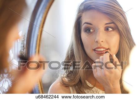 Picture - Young woman applying lipstick in mirror. Fotosearch
