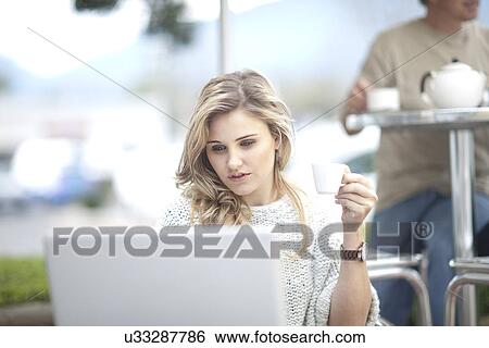 Stock Photograph - Young woman at cafe with coffee, using laptop. Fotosearch