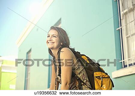 Young woman carrying backpack, standing outside painted house View Large Photo Image Stock Image - Young woman carrying backpack, standing outside painted house. Fotosearch