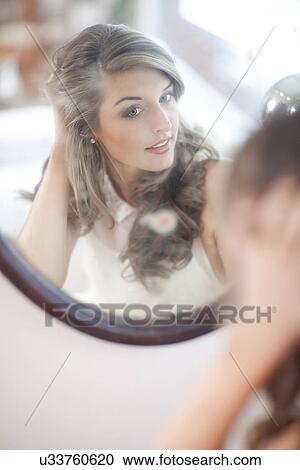 Young woman checking herself in wall mirror View Large Photo Image Stock Image - Young woman checking herself in wall mirror. Fotosearch