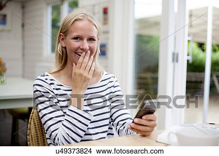 Picture - Young woman in cafe laughing at mobile phone. Fotosearch