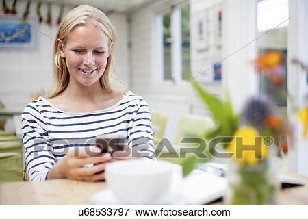 Young woman in cafe looking at mobile phone View Large Photo Image Stock Photo - Young woman in cafe looking at mobile phone. Fotosearch