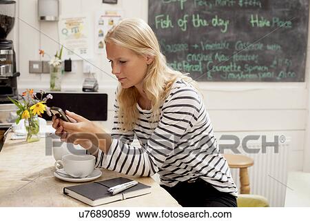 Stock Photo - Young woman in cafe reading message mobile phone. Fotosearch