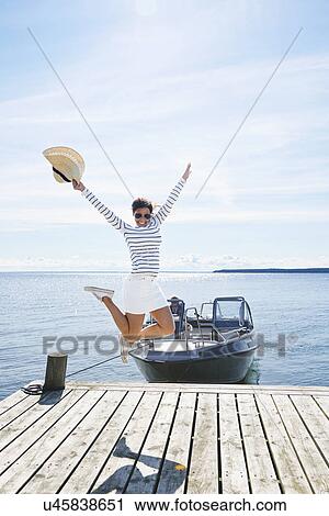Stock Image - Young woman leaping mid air on pier, Gavle, Sweden. Fotosearch