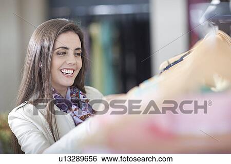 Stock Photograph - Young woman looking at clothes on rail in shop. Fotosearch