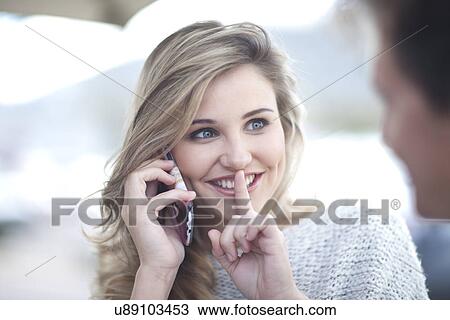 Stock Image - Young woman on phonecall with finger to lips. Fotosearch
