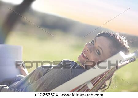 Picture - Young woman reclining in deck chair with book. Fotosearch