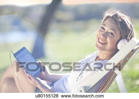 Young woman reclining in deck chair with digital tablet View Large Photo Image Stock Photo - Young woman reclining in deck chair with digital tablet. Fotosearch