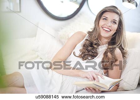 Stock Photography - Young woman reclining on sofa with book. Fotosearch