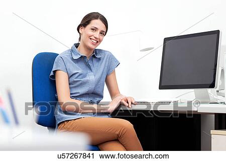 Young woman sitting at desk in office View Large Photo Image Stock Image - Young woman sitting at desk in office. Fotosearch
