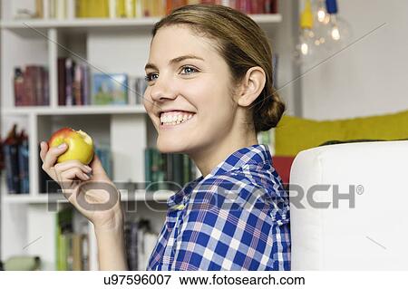 Stock Photo - Young woman sitting on floor eating an apple. Fotosearch