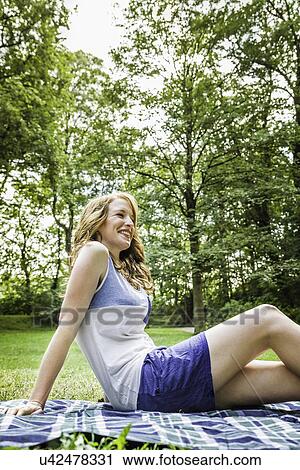 Young woman sitting on picnic blanket in park View Large Photo Image Stock Image - Young woman sitting on picnic blanket in park. Fotosearch