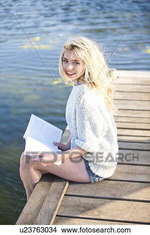 Picture - Young woman sitting on pier holding book. Fotosearch