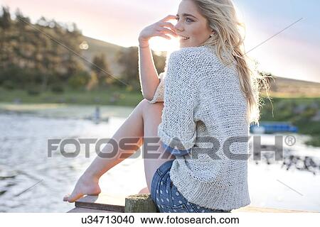 Stock Image - Young woman sitting on pier. Fotosearch