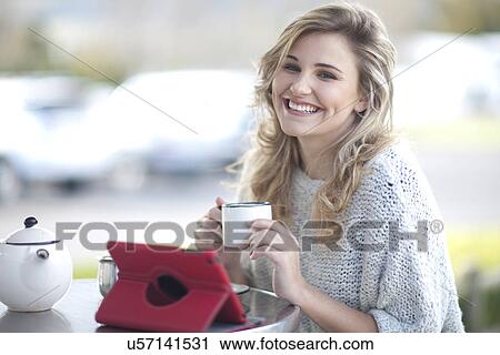 Young woman sitting outside cafe with cup of coffee and digital tablet View Large Photo Image Stock Image - Young woman sitting outside cafe with cup of coffee and digital tablet. Fotosearch