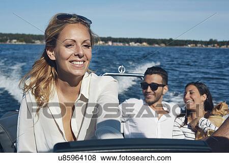 Stock Photo - Young woman steering boat with friends in background, Gavle, Sweden. Fotosearch