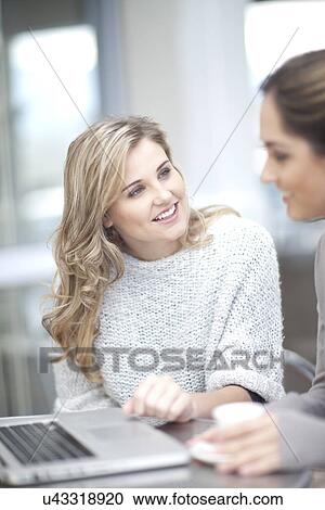 Stock Image - Young women at cafe with coffee, using laptop. Fotosearch