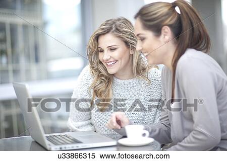 Stock Photography - Young women at cafe with coffee, using laptop. Fotosearch