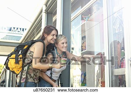 Stock Image - Young women pointing through shop window. Fotosearch
